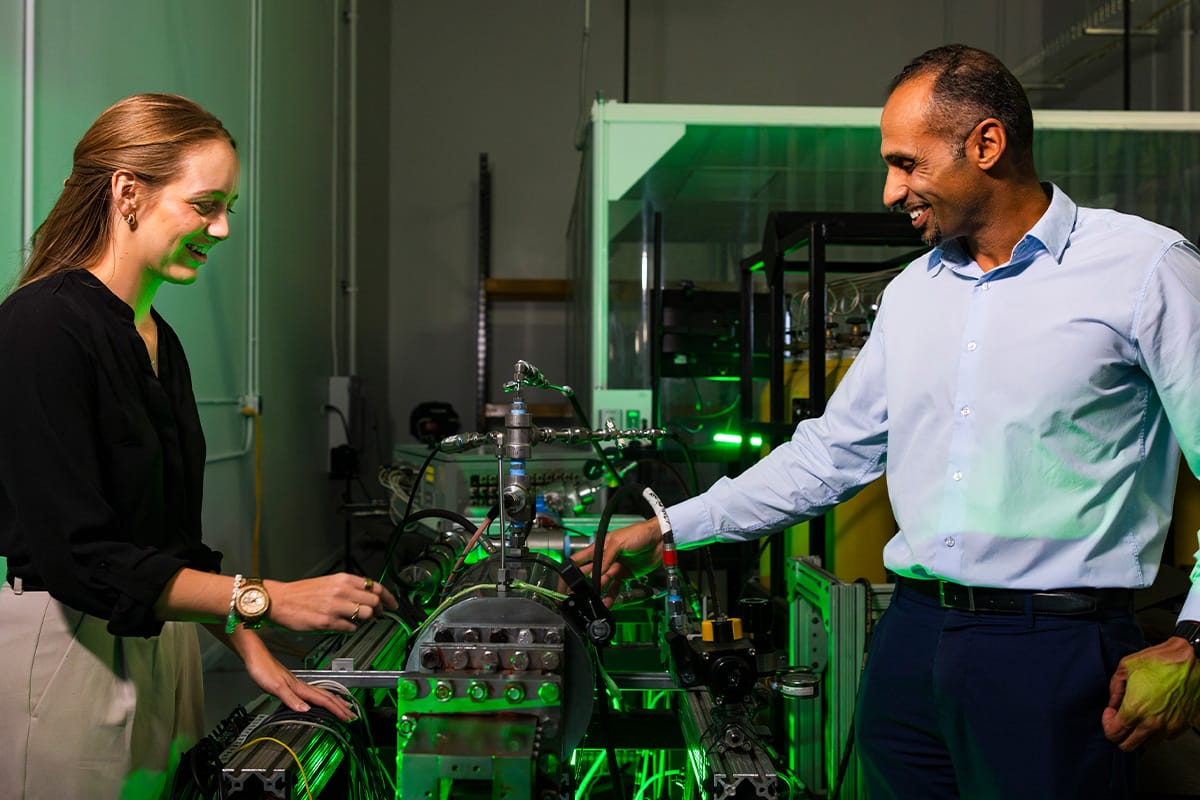 Trustee Chair Professor of Mechanical and Aerospace Engineering Kareem Ahmed and a student stands beside a propulsion device, surrounded by wiring and equipment used for hypersonic research at the UCF HyperSpace Center.
