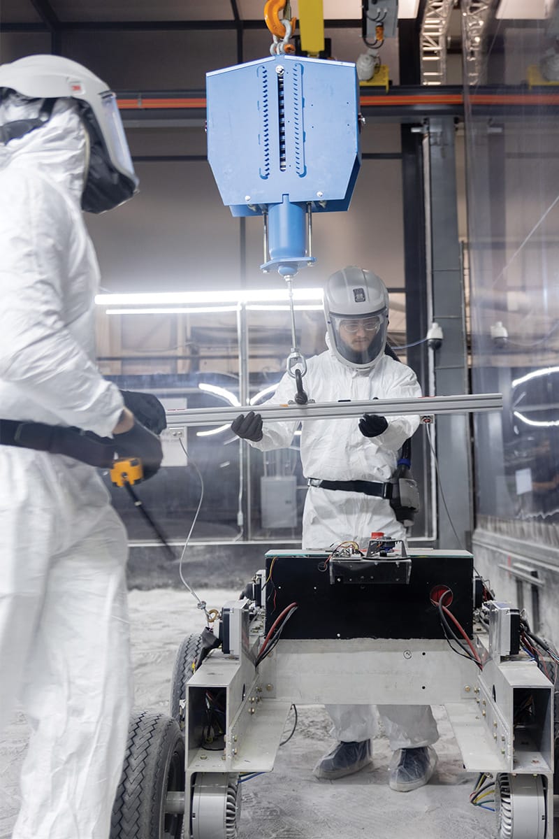 Two researchers test a rover on the world’s largest simulated lunar surface — the Lunar Highland Regolith Test Bin — located at UCF’s Exolith Lab.
