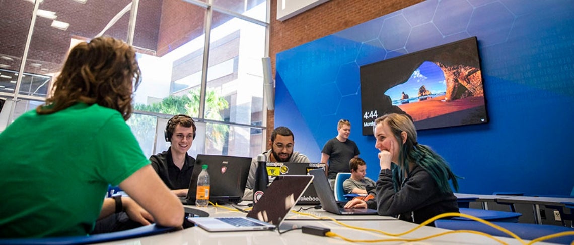 Students smiling and working on their computers during the UCF Cyber Hackathon